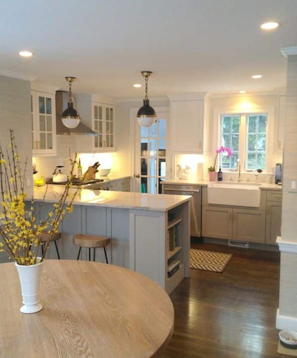 Modern kitchen with white cabinets, island, pendant lights, and flowers, featuring a cozy dining area and wooden flooring.