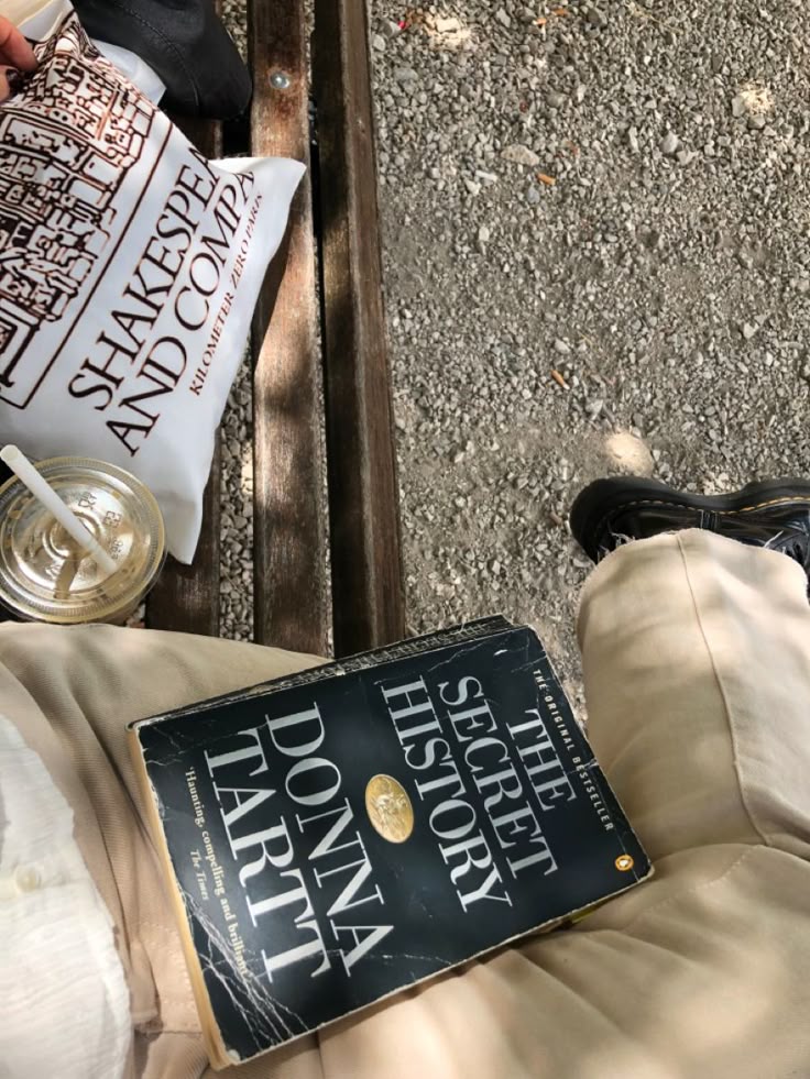Lovely things Book The Secret History on a lap, beside iced coffee and Shakespeare & Co. tote, on a park bench. | Sky Rye Design Book The Secret History on a lap, beside iced coffee and Shakespeare & Co. tote, on a park bench.