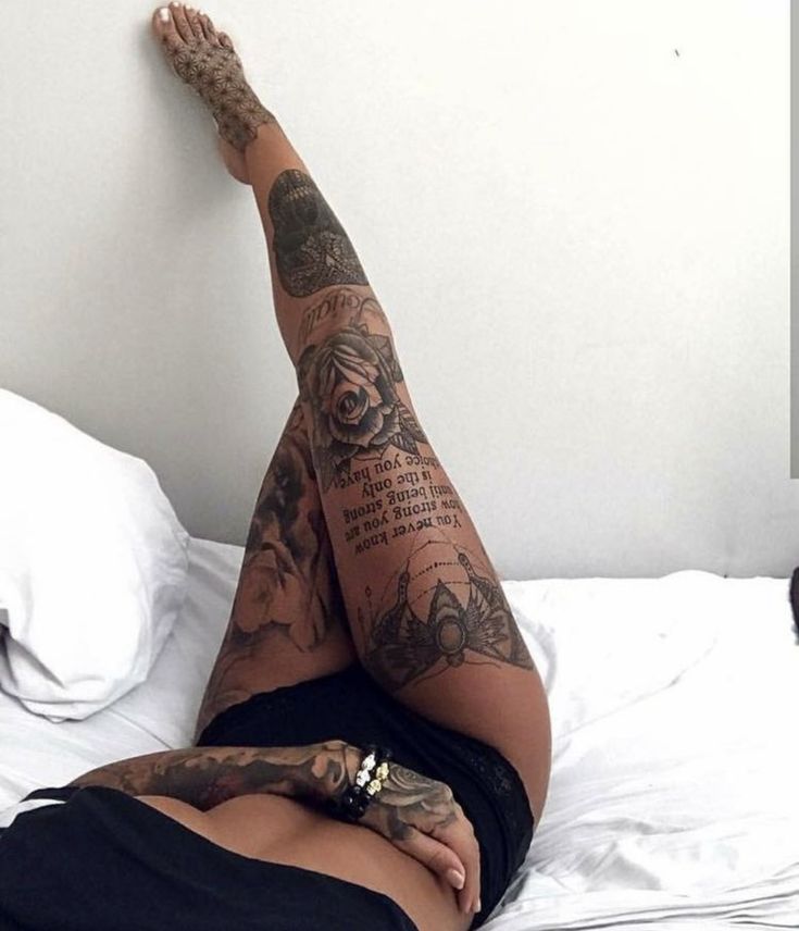 M Tattooed leg artfully displayed on bed with floral and text designs. Elegant body ink showcasing intricate details. | Sky Rye Design Tattooed leg artfully displayed on bed with floral and text designs. Elegant body ink showcasing intricate details.