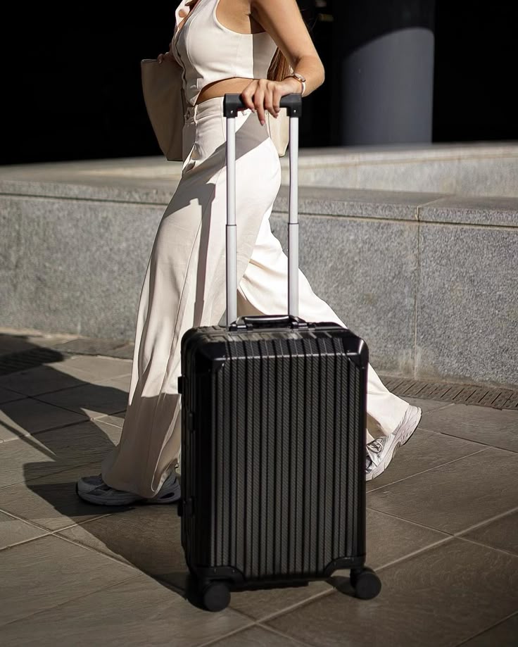Person in beige outfit walking with a black suitcase in urban setting. Travel and style concept.