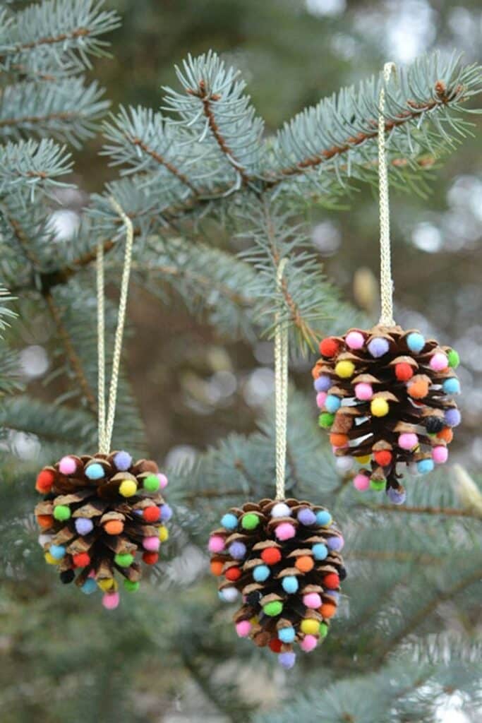 Colorful pom-pom pinecone ornaments hanging on a tree branch, perfect for festive Christmas decor.