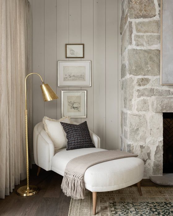 Cozy reading nook with a white chaise, gold floor lamp, and textured stone accent wall for serene relaxation.