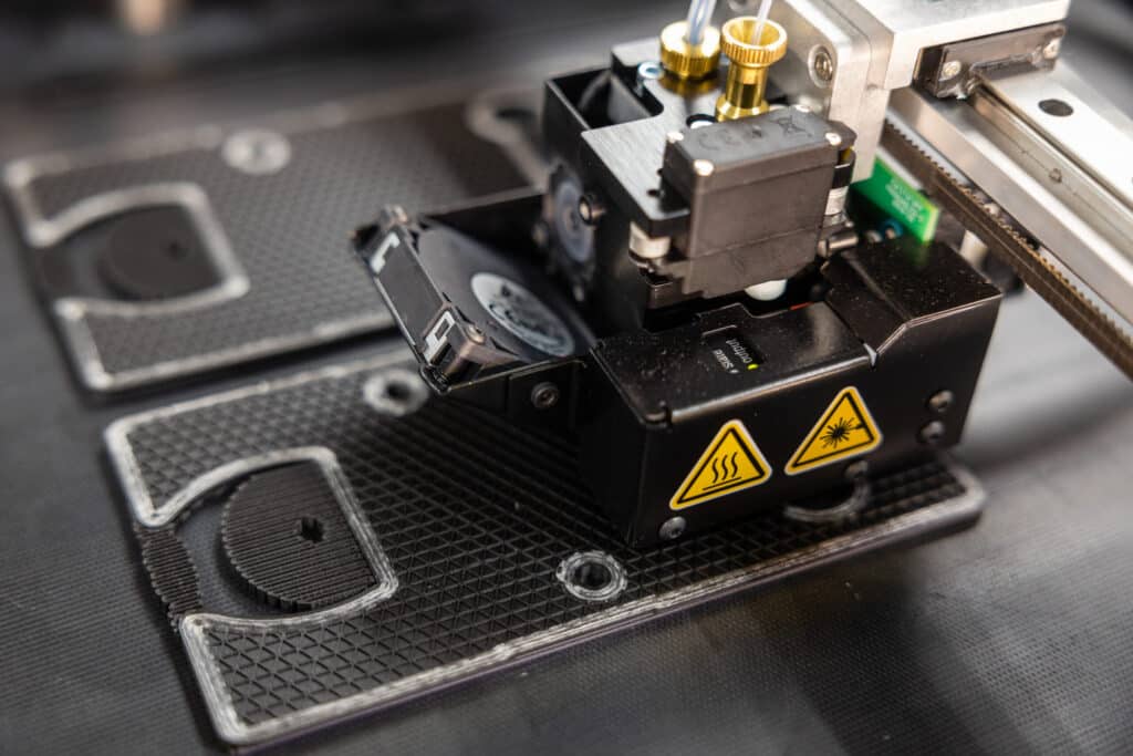 Markforged-Printer-Printing-scaled Close-up of a 3D printer in action, showing detailed printing head and filament layers on the printing bed. | Sky Rye Design Close-up of a 3D printer in action, showing detailed printing head and filament layers on the printing bed.