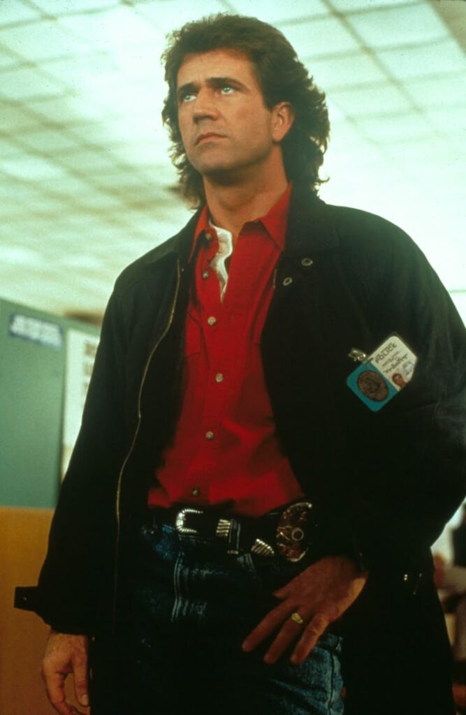 Man in a red shirt and dark jacket looking determined, with an ID badge on display.