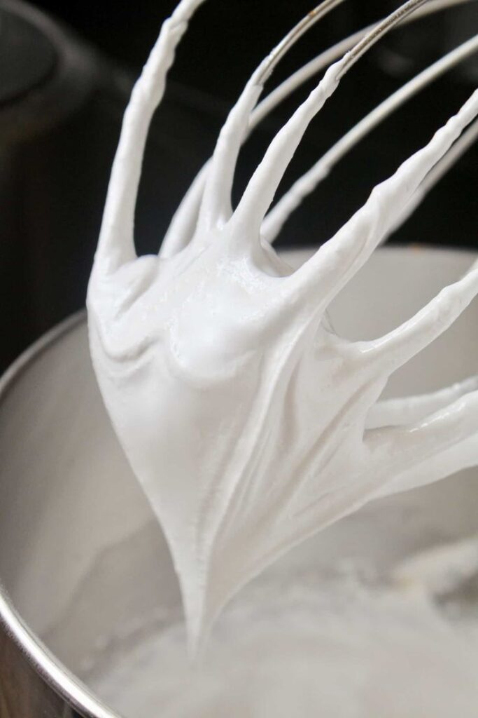 Whisk with stiff peaks of whipped cream in stainless steel bowl, perfect for baking and dessert recipes.