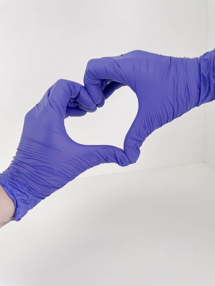 Two hands in purple gloves form a heart shape, symbolizing care and support in a medical or healthcare setting.