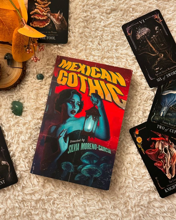 Mexican Gothic - a gothic horror novel by Silvia Moreno-Garcia _ Cup of Kee Mexican Gothic book by Silvia Moreno-Garcia surrounded by tarot cards on a textured cream surface. | Sky Rye Design Mexican Gothic book by Silvia Moreno-Garcia surrounded by tarot cards on a textured cream surface.