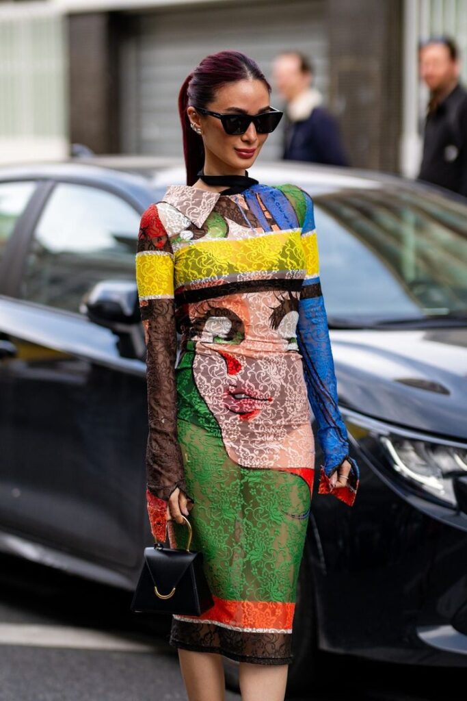 Millennial fashion trends that are coming back in 2025 2026 - karyastreetstyle Fashion-forward woman in a colorful, artistic dress with sunglasses and a handbag on a city street. | Sky Rye Design Fashion-forward woman in a colorful, artistic dress with sunglasses and a handbag on a city street.