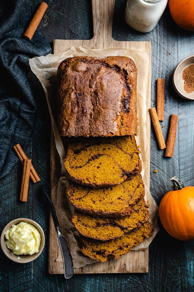 Moist Pumpkin Bread with Cinnamon-Sugar Swirl - Host The Toast Sliced pumpkin bread on a wooden board with cinnamon sticks and butter, perfect for autumn recipes. | Sky Rye Design Sliced pumpkin bread on a wooden board with cinnamon sticks and butter, perfect for autumn recipes.