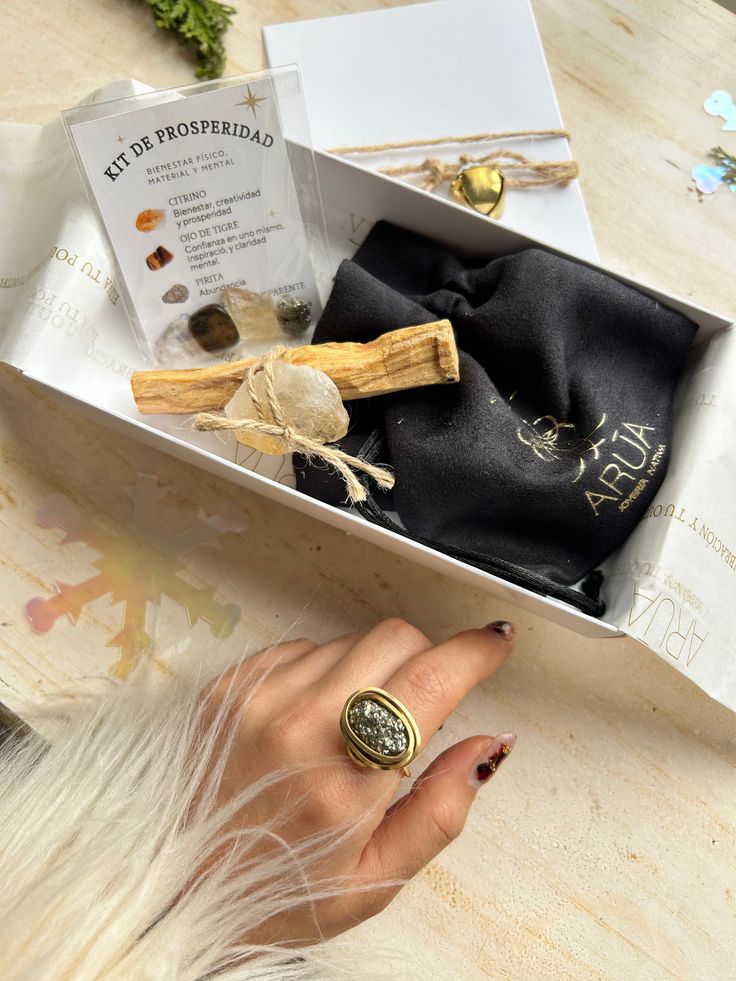 Prosperity kit with crystals, wooden stick, and ring in gift box on light surface.