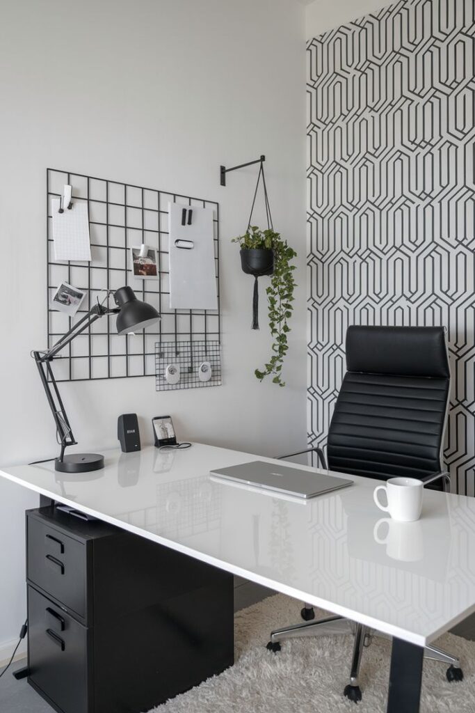 Modern home office with geometric wallpaper, sleek desk, laptop, and cozy chair. Stylish workspace setup.