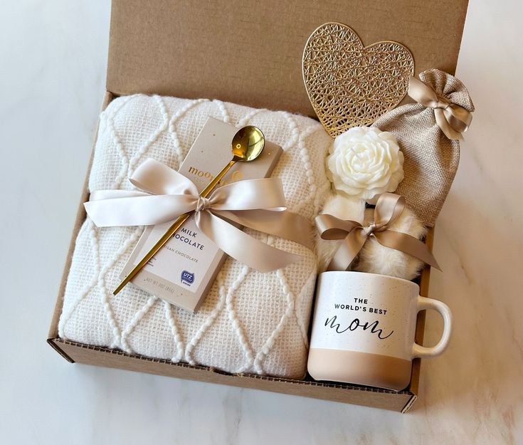 Gift box with a cozy blanket, chocolate, World's Best Mom mug, gold spoon, and decorative items. Perfect for Mother's Day.