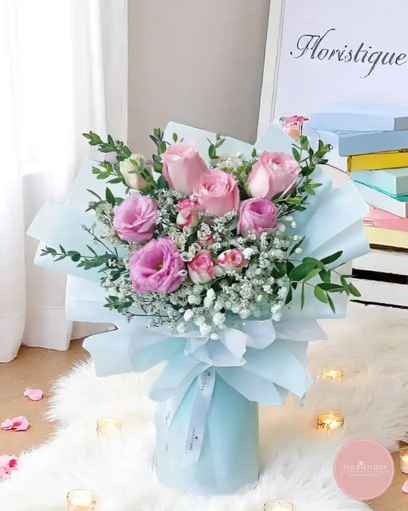 Elegant pink and white floral bouquet in blue wrapping on fluffy white rug, surrounded by candles for a cozy ambiance.