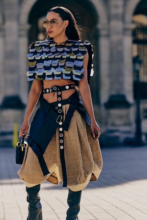 Trendy woman in bold geometric outfit with knee-high boots, sunglasses, and handbag, strolling confidently on city street.