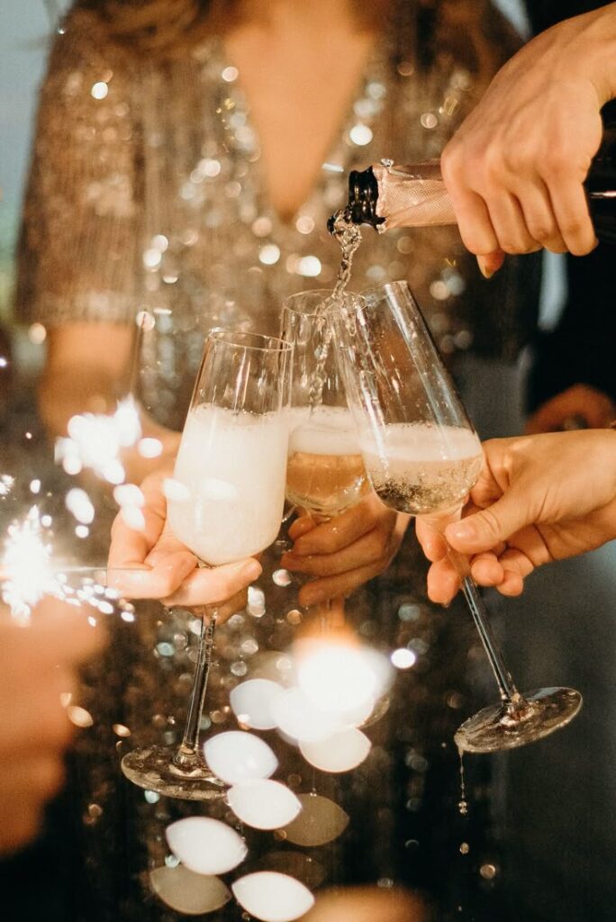 NYE Champagne being poured into glasses at a festive celebration with sparklers and bokeh lights in the background. | Sky Rye Design Champagne being poured into glasses at a festive celebration with sparklers and bokeh lights in the background.