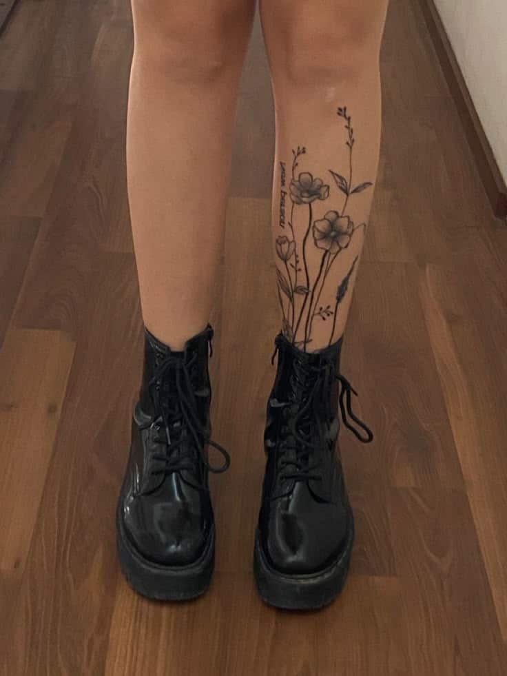 New person same old mistakes_ Leg with floral tattoo wearing black leather boots on a wooden floor. | Sky Rye Design Leg with floral tattoo wearing black leather boots on a wooden floor.