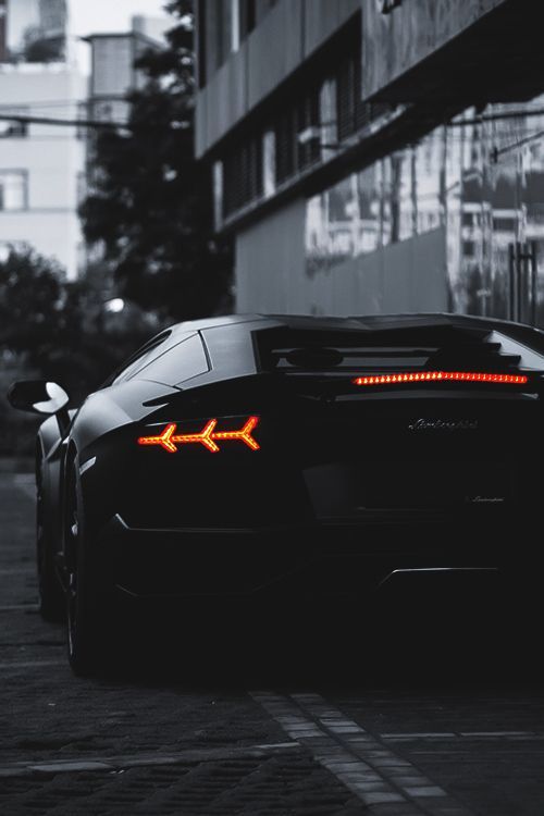 Sleek black sports car with illuminated taillights in urban setting, highlighting luxury and modern design.