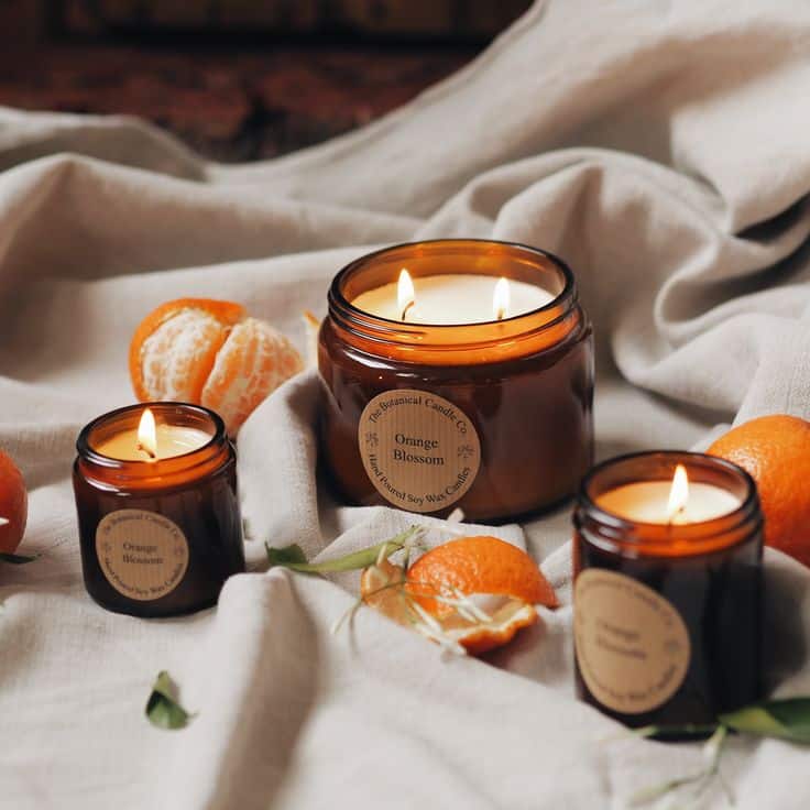 Orange Blossom Scented Soy Candles in Amber Jars Orange Blossom candles in amber jars with fresh tangerines on soft fabric, creating a cozy and aromatic atmosphere. | Sky Rye Design Orange Blossom candles in amber jars with fresh tangerines on soft fabric, creating a cozy and aromatic atmosphere.