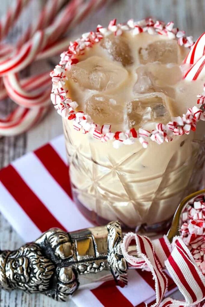 Festive holiday cocktail with candy cane rim, ice cubes, and a creamy drink in a decorative glass.