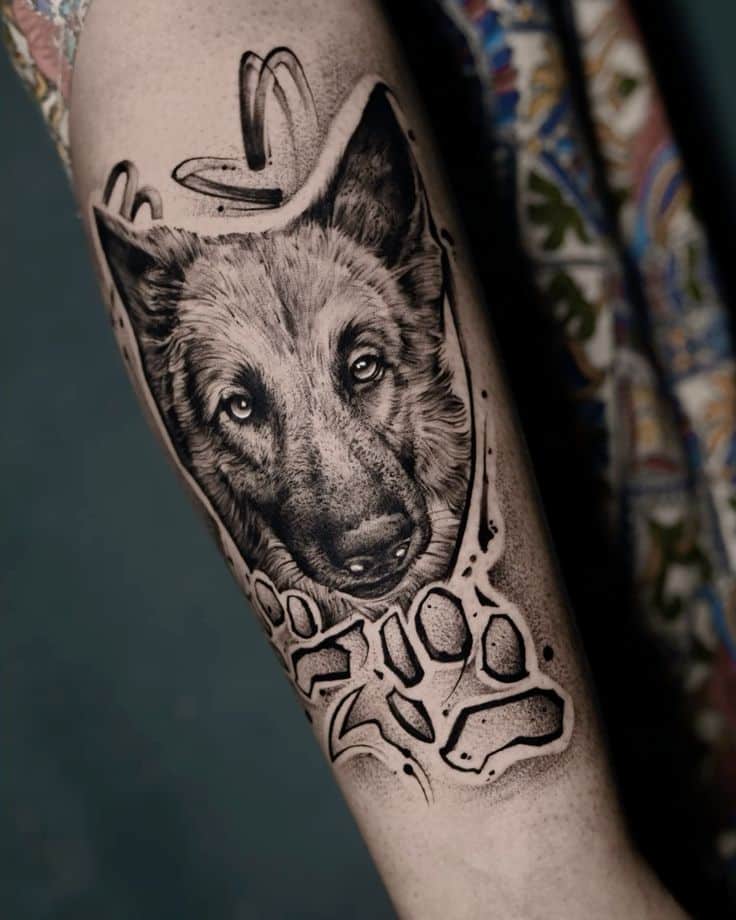 Realistic dog tattoo on forearm with intricate shading and paw print design near colorful patterned fabric background.