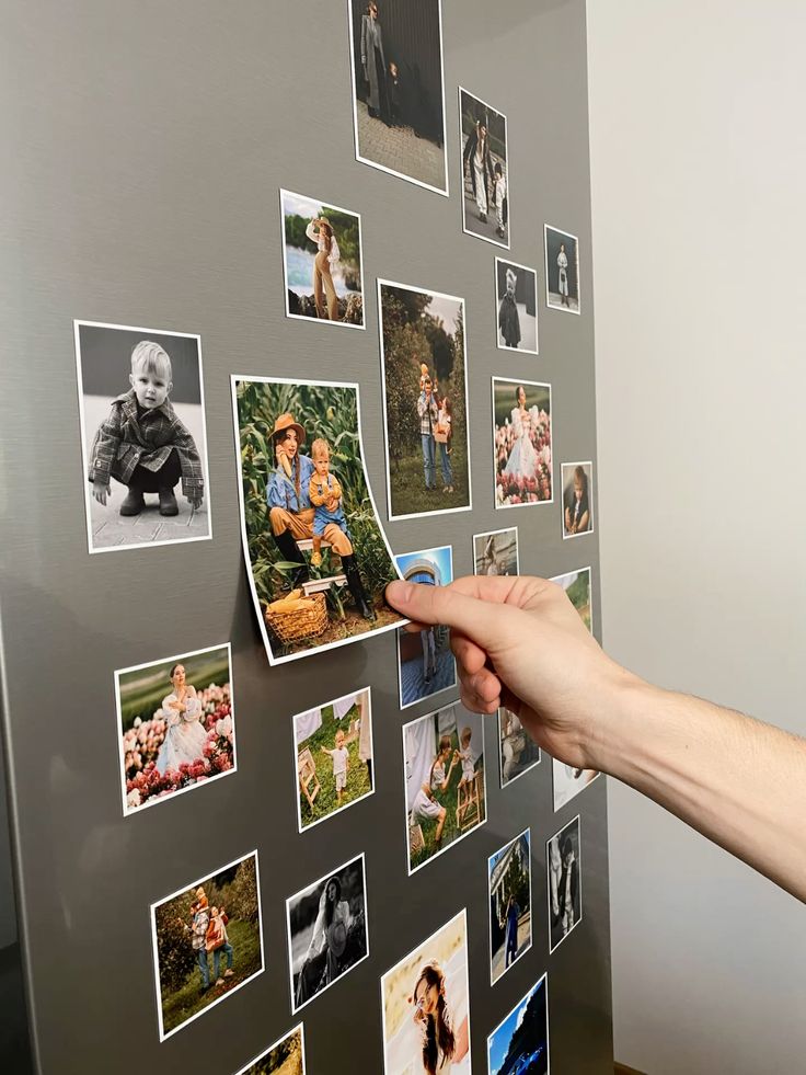 Hand arranging family photo collage on a gray wall, showcasing various family moments and memories.