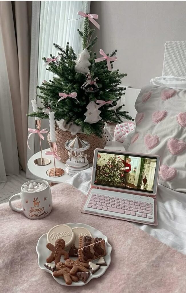 Pink Christmas room decor_ Cozy Christmas scene with a small decorated tree, laptop, hot cocoa, and cookies on a pink blanket. | Sky Rye Design Cozy Christmas scene with a small decorated tree, laptop, hot cocoa, and cookies on a pink blanket.