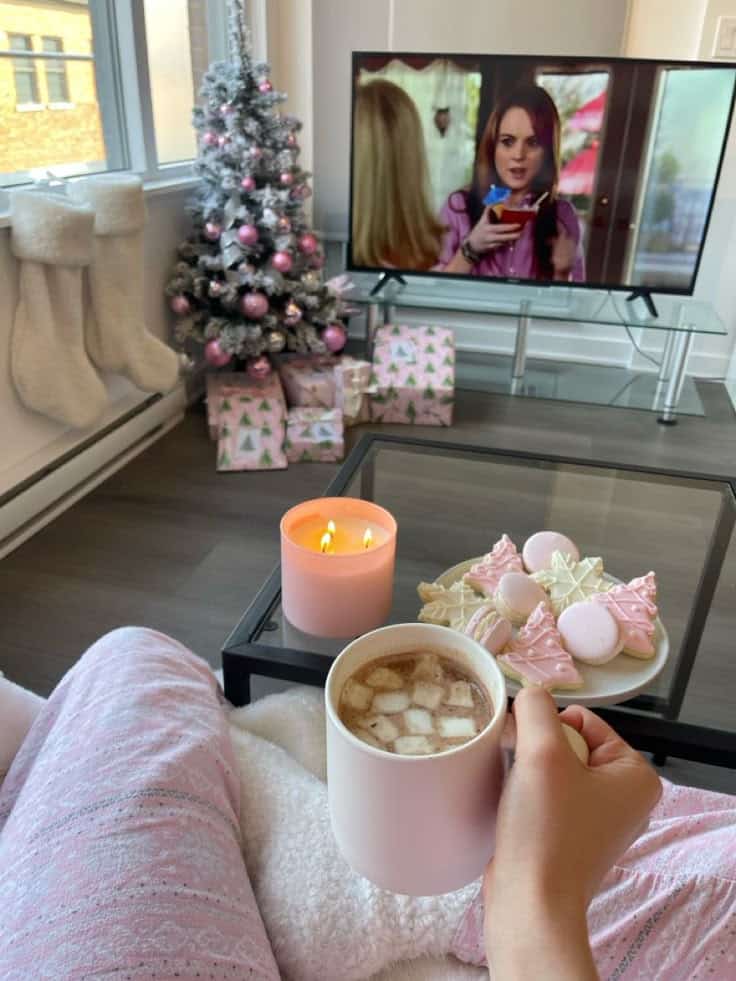 Pink Christmas Cozy holiday scene with hot cocoa, festive cookies, a lit candle, Christmas tree, and TV in a warm living room. | Sky Rye Design Cozy holiday scene with hot cocoa, festive cookies, a lit candle, Christmas tree, and TV in a warm living room.