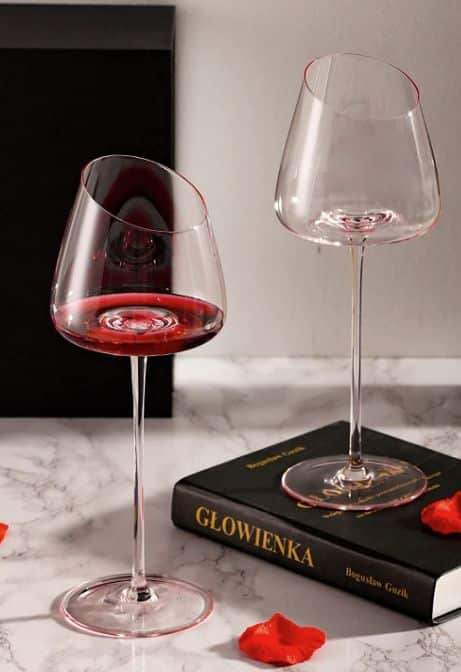 Pink Crystal Wine Glass Two modern wine glasses, one with red wine, on a marble surface beside a book and rose petals. | Sky Rye Design Two modern wine glasses, one with red wine, on a marble surface beside a book and rose petals.