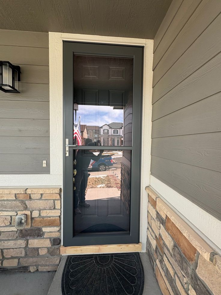 Platinum Rollscreen - OVERSIZED - Black _ Antique Brass - Curved Front door with a glass storm door, reflecting a suburban street scene with houses and a parked car. | Sky Rye Design Front door with a glass storm door, reflecting a suburban street scene with houses and a parked car.