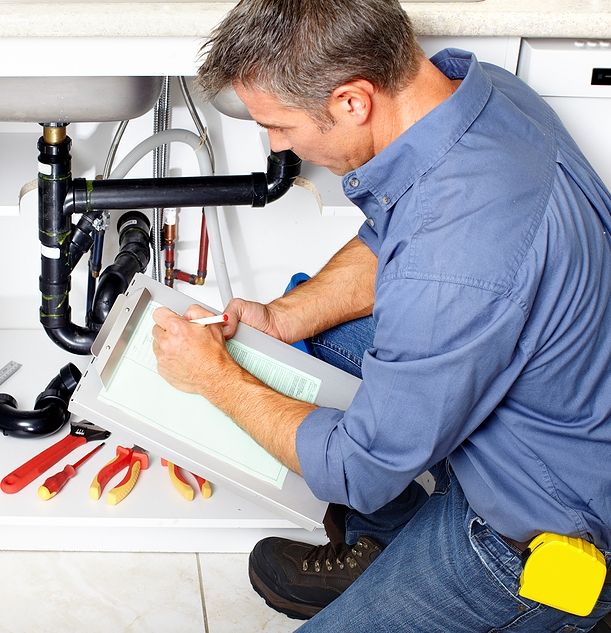 Man inspecting plumbing under sink and making notes; clipboard, tools visible.