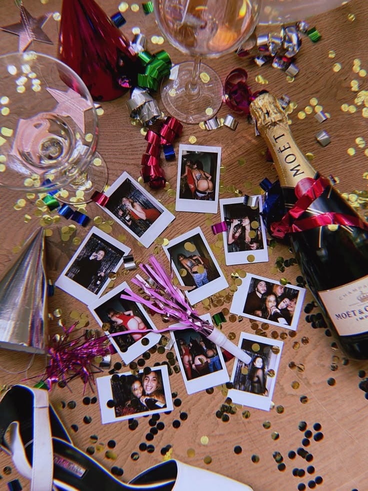 Polaroid Celebration scene with champagne, photos, confetti, party hats, and streamer on a wooden table. | Sky Rye Design Celebration scene with champagne, photos, confetti, party hats, and streamer on a wooden table.
