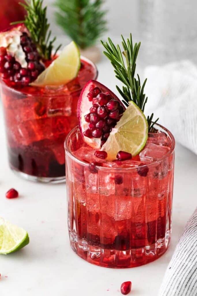 Refreshing pomegranate cocktail with lime and rosemary garnish, perfect for festive occasions and celebrations.