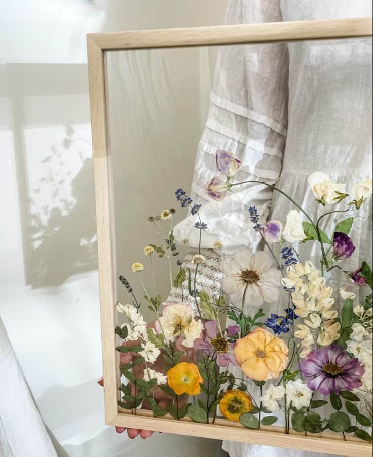 Pressed wedding bouquet Framed pressed flowers held by a person in a white dress, showcasing colorful botanical art against a bright background. | Sky Rye Design Framed pressed flowers held by a person in a white dress, showcasing colorful botanical art against a bright background.