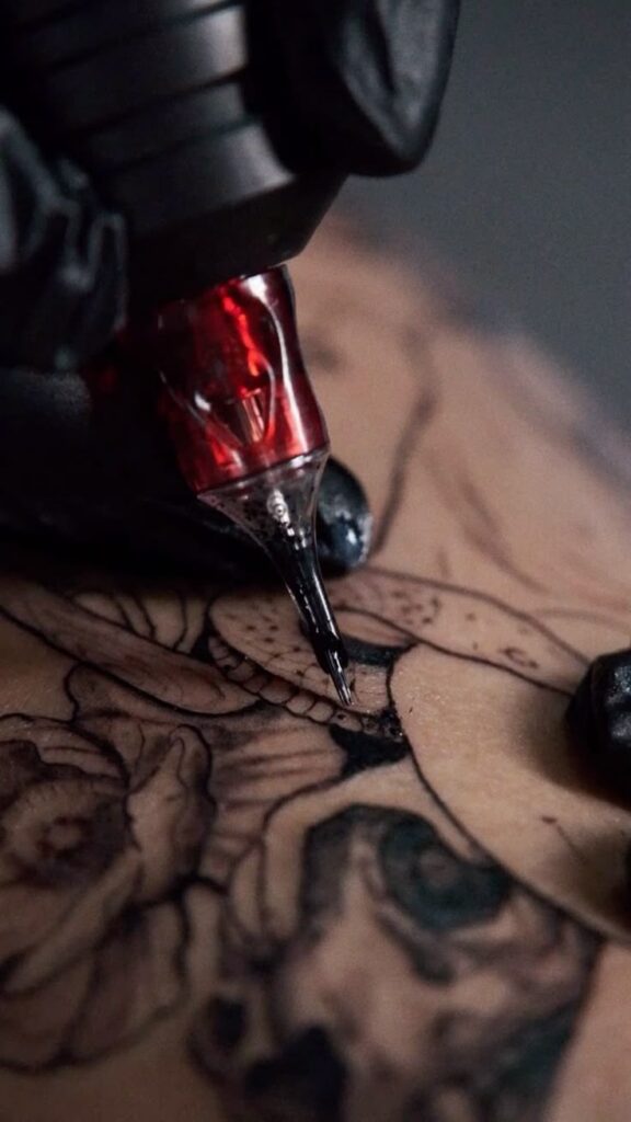 Tattoo artist using machine to ink detailed design on skin, showcasing intricate black lines.