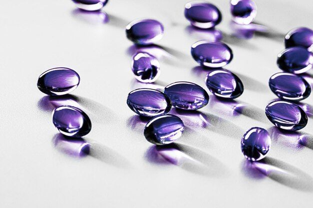 Purple gelatin capsules scattered on a white surface, casting soft shadows. Perfect for health and wellness content.