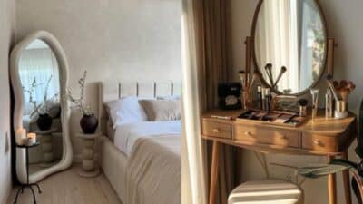 Modern bedroom with cozy bed, large mirror, and elegant makeup vanity with brushes and cosmetics. Minimalist decor style.