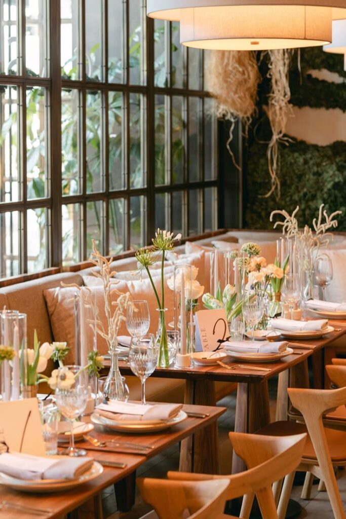 Elegant restaurant table setup with floral decorations and soft lighting by large windows.
