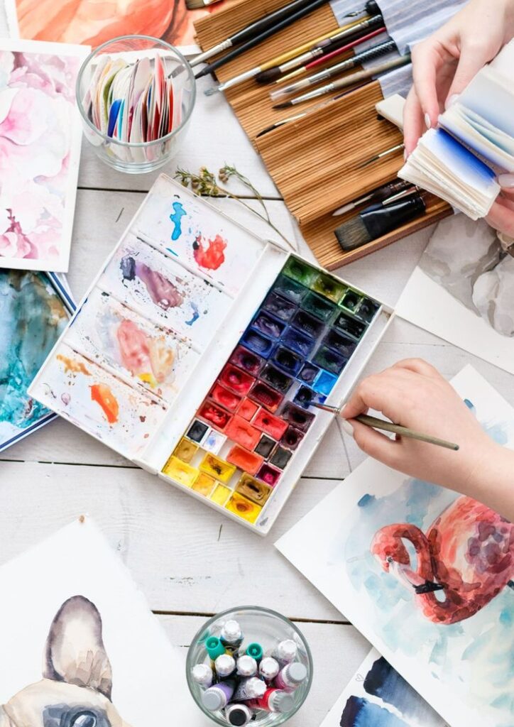 Artist painting with watercolor palette and brushes on a desk, creating vibrant artwork.