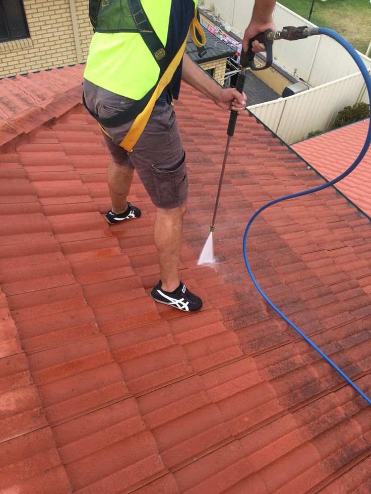Worker pressure washing a red tile roof for maintenance and cleaning.