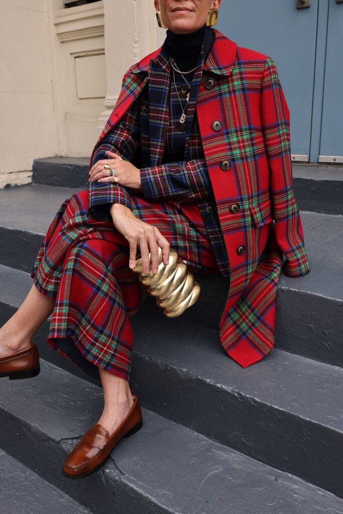 STYLING FALL BODEN IN NYC Stylish woman in red plaid suit with gold accessories sits on stairs, showcasing modern fashion. | Sky Rye Design Stylish woman in red plaid suit with gold accessories sits on stairs, showcasing modern fashion.