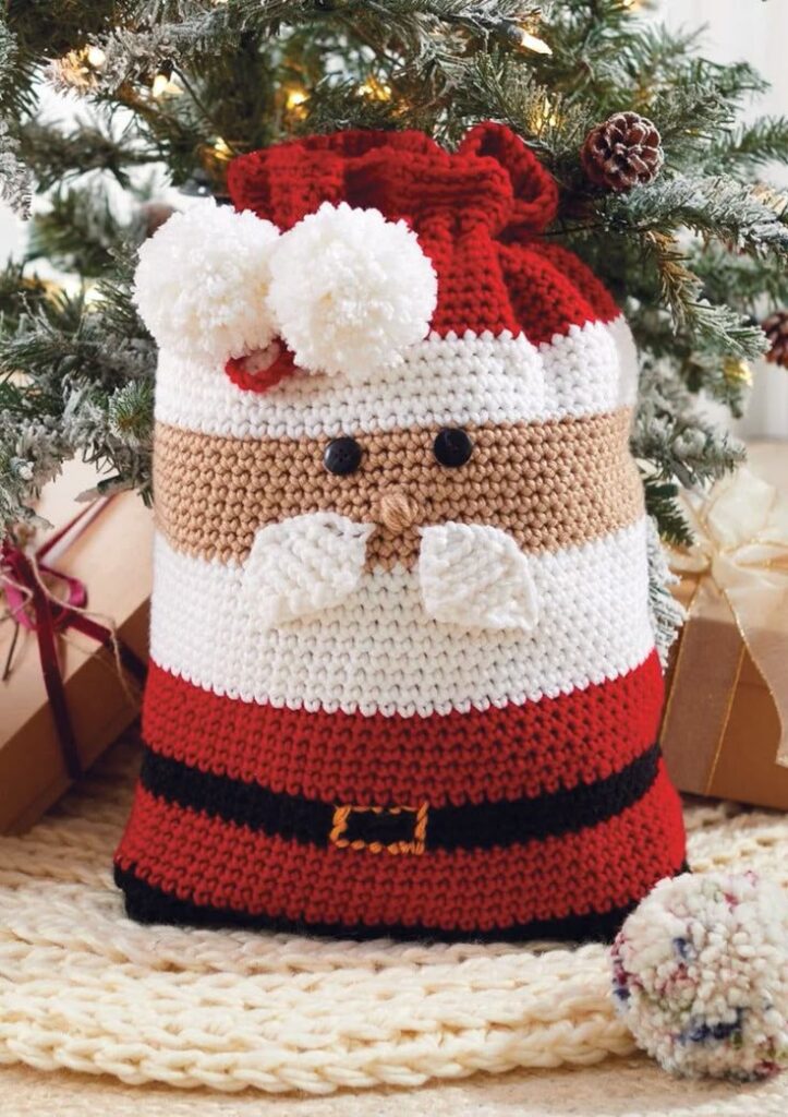 Santa Gift Bag Crochet Kit Crocheted Santa gift bag under a decorated Christmas tree with gifts, enhancing festive holiday decor. | Sky Rye Design Crocheted Santa gift bag under a decorated Christmas tree with gifts, enhancing festive holiday decor.