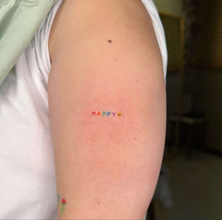 Colorful HAPPY tattoo with a smiley face on a person's arm, emphasizing positivity and vibrant design.