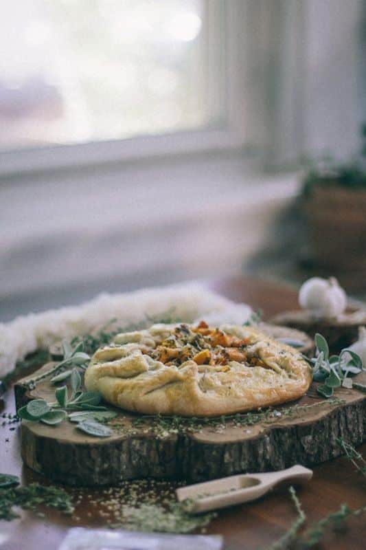Savory Butternut Squash Galette Rustic vegetable galette on a wooden board with fresh herbs, next to a window. | Sky Rye Design Rustic vegetable galette on a wooden board with fresh herbs, next to a window.