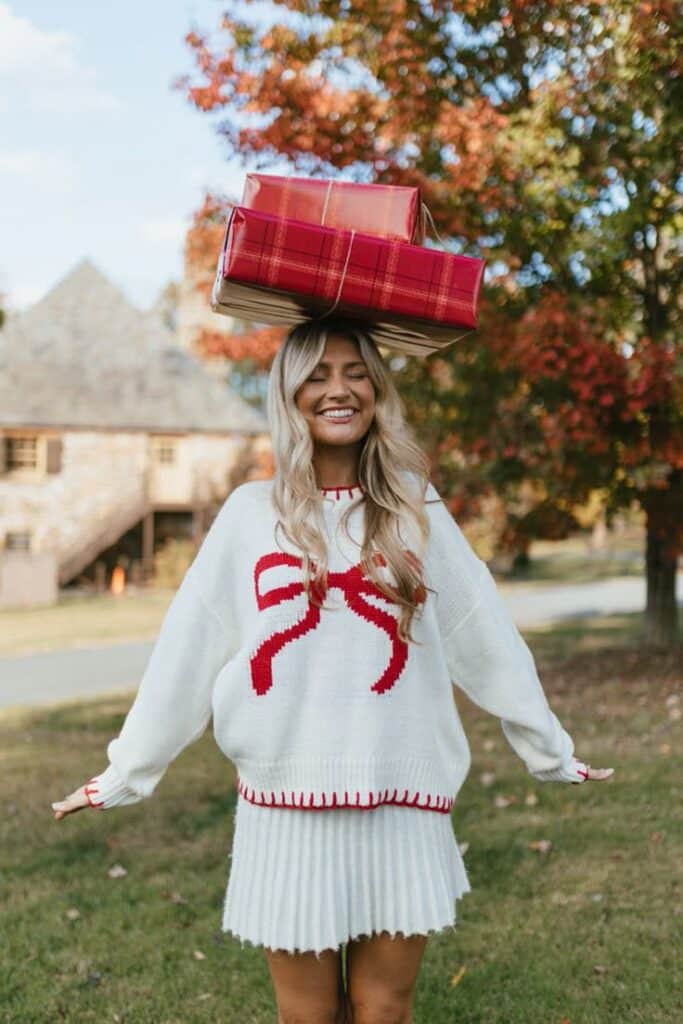 Sawyer Sweater Woman in festive sweater balances wrapped gifts on her head, smiling, with autumn trees in the background. | Sky Rye Design Woman in festive sweater balances wrapped gifts on her head, smiling, with autumn trees in the background.