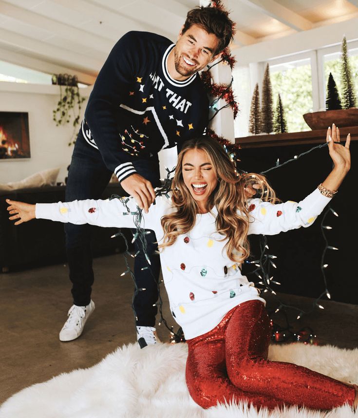 Couple enjoying festive holiday decor indoors, smiling and playfully tangled in Christmas lights.