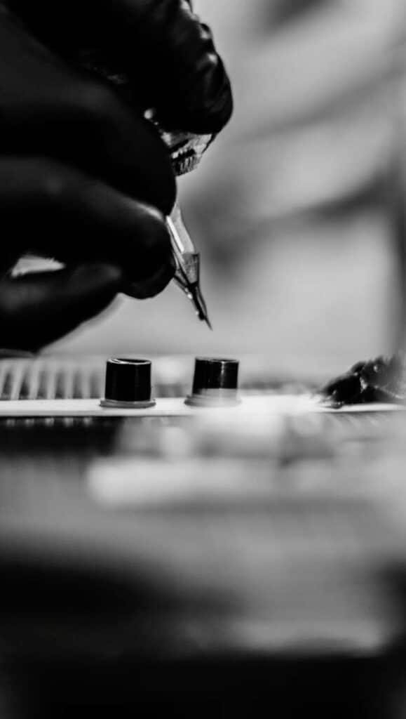 Close-up of a tattoo artist's hand with a needle and ink, in black and white.