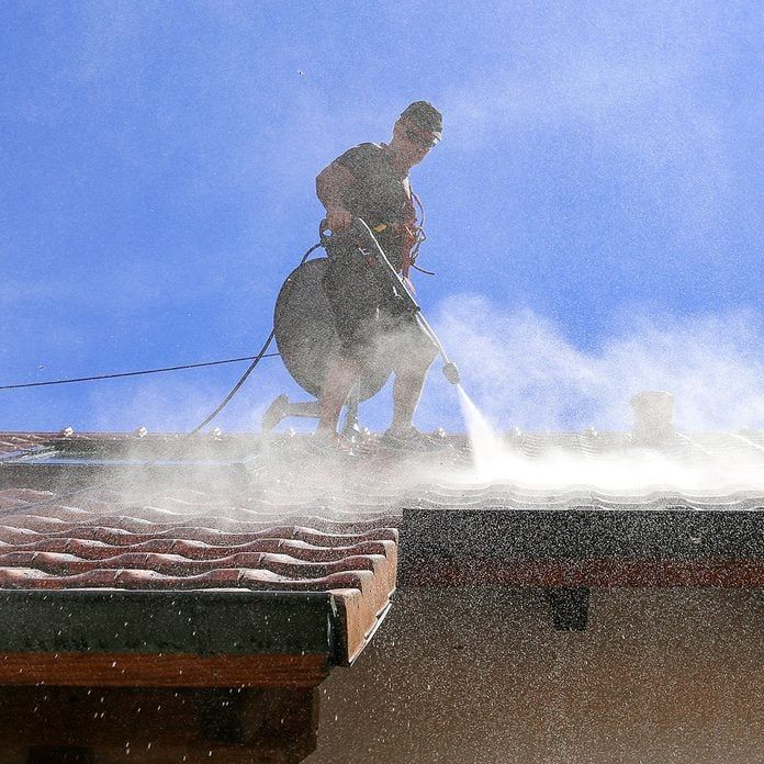 Worker power-washing roof tiles on a sunny day, removing dirt and debris for clean maintenance.