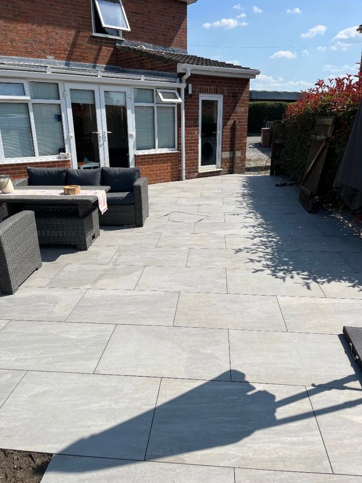 Modern patio with light gray tiles, wicker furniture, and a red brick exterior under a clear blue sky.