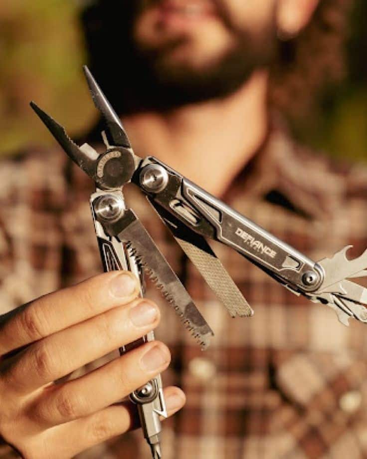 Person holding a multi-tool with various attachments, outdoor background.