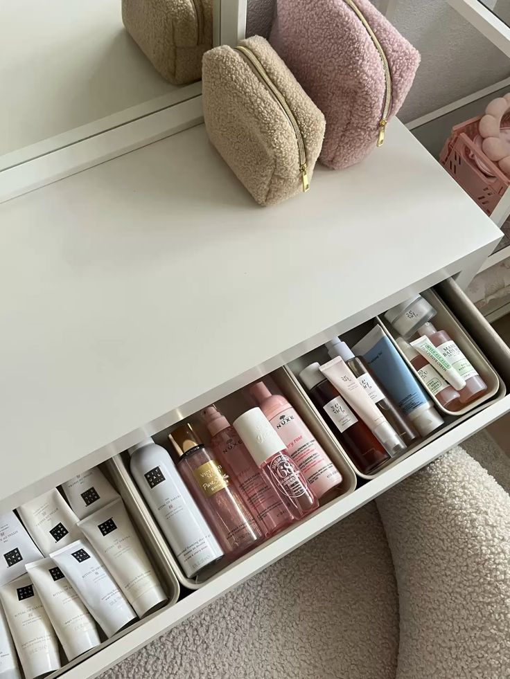 Vanity table with organized skincare products in drawers and two plush makeup bags on top.